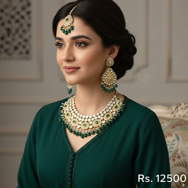 Gold-plated bridal jewelry set with green Kundan stones and pearls, including a necklace, jhumka earrings, and tikka, priced at Rs. 12500
