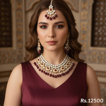 Gold-plated bridal jewelry set with red Kundan stones and pearls, including a necklace, jhumka earrings, and tikka, priced at Rs. 12500