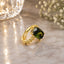 22K Gold-Tone Dark Olive Green CZ Solitaire Nugget Split Band Statement Ring on cream marble surface with crystal vase bokeh light and white baby's breath flowers backdrop