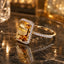 22K Gold-Tone Emerald-Cut Citrine CZ Rectangular Halo & Pavé Shoulder Cocktail Ring on dark brown marble surface with crystal bokeh gold light orbs and champagne gold backdrop