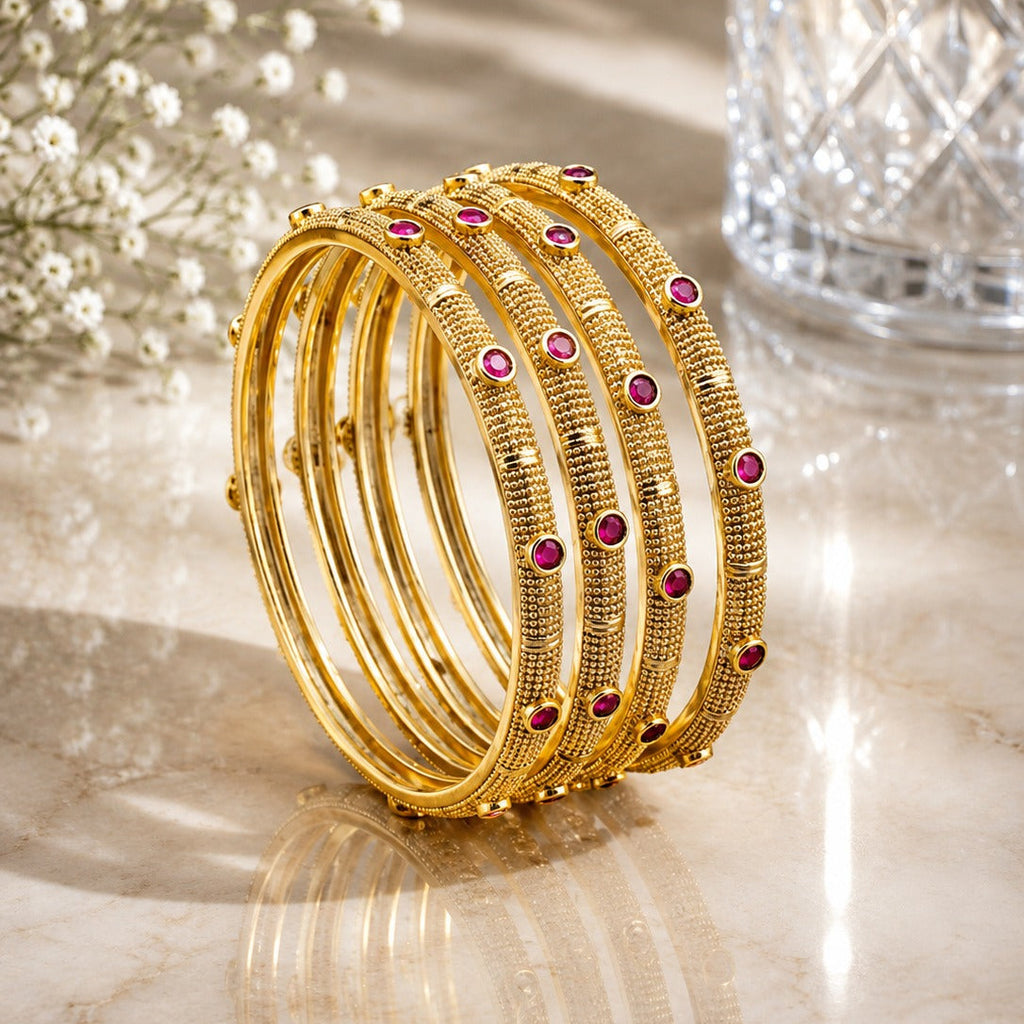 22K Gold-Tone Micro-Granule Textured Ruby Red Round CZ Pakistani Bridal Bangle Set of 4 stacked on marble surface with white baby's breath flowers and crystal glass vase backdrop