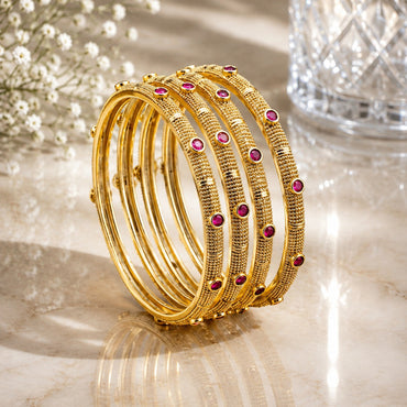 22K Gold-Tone Micro-Granule Textured Ruby Red Round CZ Pakistani Bridal Bangle Set of 4 stacked on marble surface with white baby's breath flowers and crystal glass vase backdrop