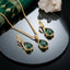 22K Gold-Tone Pear Emerald CZ Halo Pendant Necklace & Huggie Drop Earrings Jewelry Set flat lay on black mirror surface with emerald green embroidered fabric and white quartz crystal cluster backdrop