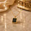 22K Gold-Tone Square Clock Face Roman Numeral Pendant Necklace on cream marble surface with champagne satin fabric and gold Mughal decorative urn backdrop