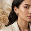 22K Gold-Tone Twisted Double Band Pear CZ Solitaire Huggie Hoop Earrings worn on South Asian female model in cream blazer with dried baby's breath flowers backdrop