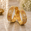 22K Gold-Tone Wide Filigree Kundan Flower & Ruby CZ Granule Bridal Kada Set of 2 on marble surface with gold lotus candle holder and white baby's breath flowers backdrop