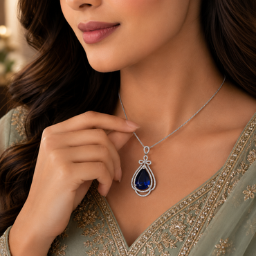 Woman wearing royal blue sapphire CZ teardrop bow pendant necklace in silver-tone styled with a sage green embroidered Pakistani formal outfit
