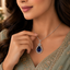 Woman wearing royal blue sapphire CZ teardrop bow pendant necklace in silver-tone styled with a sage green embroidered Pakistani formal outfit