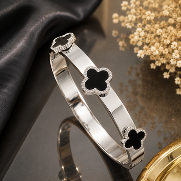 Elegant clover motif bracelet with black floral details and sparkling stone border in gold and silver finishes