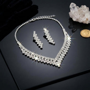 Silver-Tone Pavé White CZ V-Bib Choker Necklace & Zigzag Drop Earrings Bridal Jewelry Set flat lay on black reflective surface with white quartz crystal cluster and gold coin backdrop