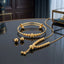 Gold Ribbed Ball Bead Tassel Necklace Bracelet Earrings Set 3 Piece in 22K gold-tone plating on black mirror surface with dark blue interior backdrop and gold glass jewellery box showing double-wire expandable bangle with ribbed gold ball beads snake chain necklace with tassel slider drop pendant and smooth round gold dome ball stud earrings with mirror reflections below