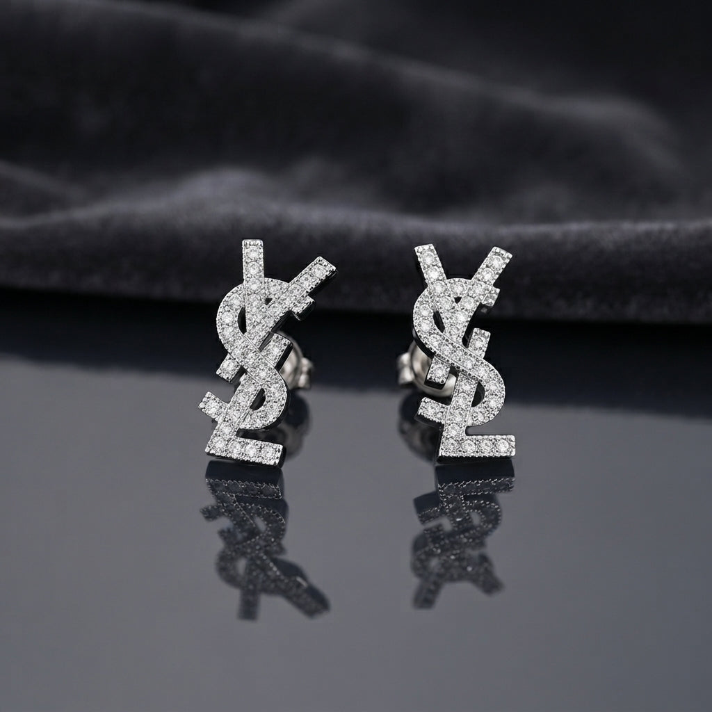 Micro Pavé CZ Monogram Letter Stud Earrings in gold-tone plating flat lay on black mirror surface with grey silk backdrop showing fully encrusted round CZ interlocking letter monogram studs with mirror reflections below