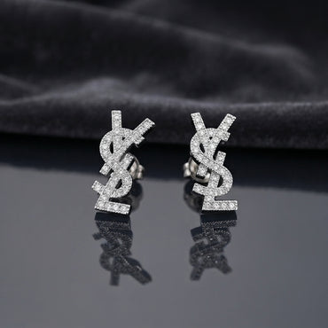 Micro Pavé CZ Monogram Letter Stud Earrings in gold-tone plating flat lay on black mirror surface with grey silk backdrop showing fully encrusted round CZ interlocking letter monogram studs with mirror reflections below