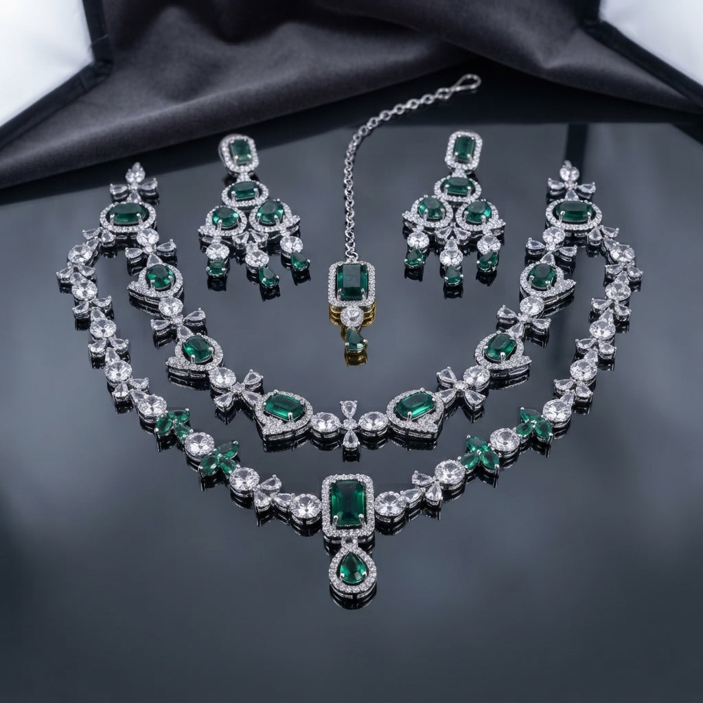 Emerald-green AD bridal jewelry set with layered necklaces, coordinating drop earrings, and maang tikka in a silver-tone finish