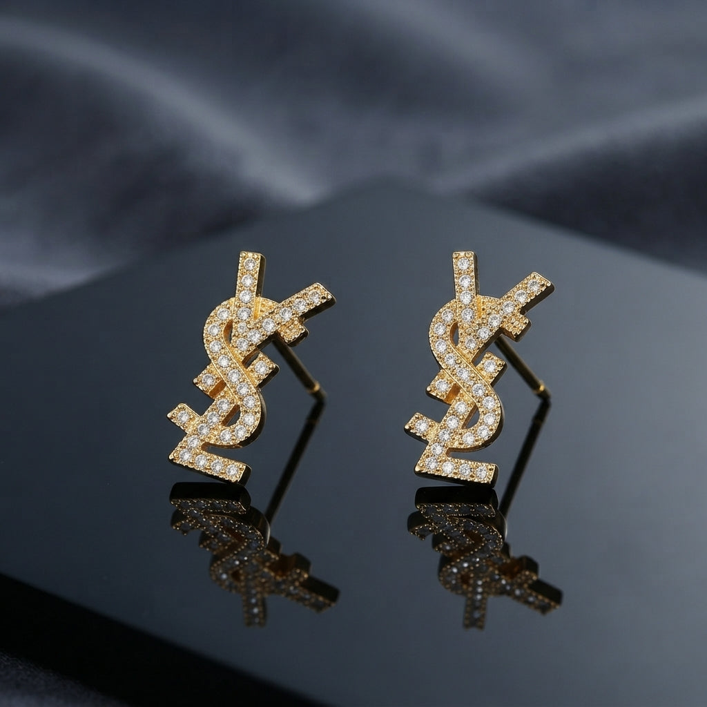 Micro Pavé CZ Monogram Letter Stud Earrings in silver-tone plating flat lay on black mirror surface with grey silk backdrop showing fully encrusted round CZ interlocking letter monogram studs with mirror reflections below