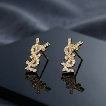 Micro Pavé CZ Monogram Letter Stud Earrings in silver-tone plating flat lay on black mirror surface with grey silk backdrop showing fully encrusted round CZ interlocking letter monogram studs with mirror reflections below