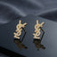 Micro Pavé CZ Monogram Letter Stud Earrings in silver-tone plating flat lay on black mirror surface with grey silk backdrop showing fully encrusted round CZ interlocking letter monogram studs with mirror reflections below