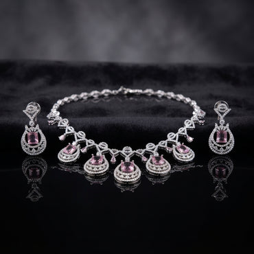 Silver Amethyst Purple CZ Emerald-Cut Teardrop Necklace and Drop Earrings Bridal Set — rhodium silver-tone 2-piece bridal set with 5-station graduating teardrop necklace featuring emerald-cut amethyst purple CZ with double concentric white CZ micro-pavé halo rings and marquise CZ bow-tie chain and matching teardrop drop earrings displayed on dark black mirror surface with charcoal satin backdrop