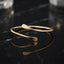 Slim gold-tone open cuff bracelet with a smooth curved band and flattened ends.