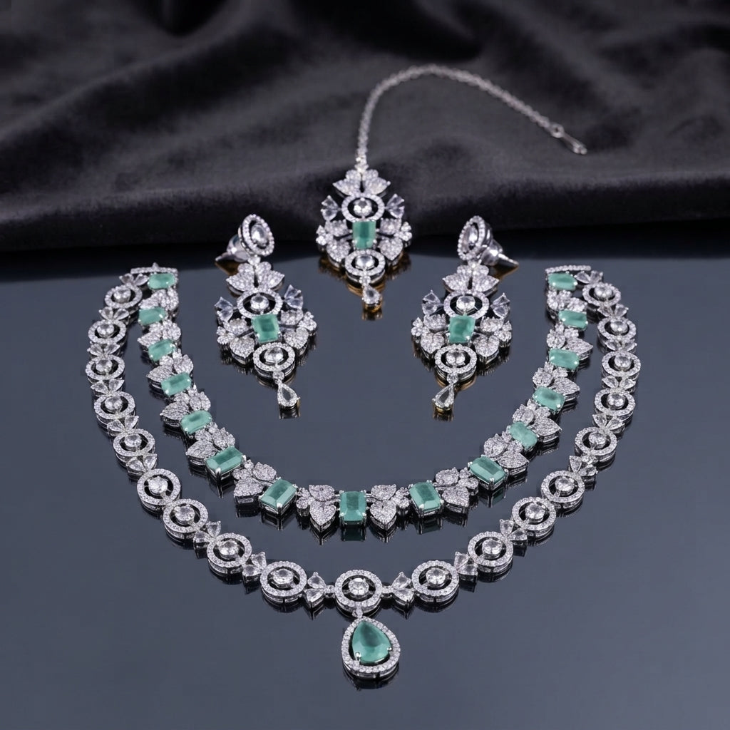 Silver-tone bridal jewelry set with emerald green stones, layered necklaces, matching drop earrings, and forehead ornament