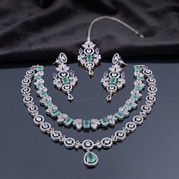 Silver-tone bridal jewelry set with emerald green stones, layered necklaces, matching drop earrings, and forehead ornament