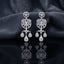 Silver CZ Medallion and Triple Pear Halo Chandelier Drop Earrings — rhodium silver-tone bridal chandelier earrings with round CZ medallion stud open Gothic arch chandelier body with trefoil pear CZ halos cruciform CZ connector and 3-drop triple pear CZ halo fringe displayed on dark black mirror surface with charcoal satin backdrop