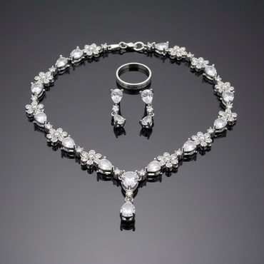 Silver jewelry set with necklace, earrings, and ring on a reflective surface