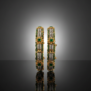 Pair of gold earrings with green and clear gemstones on a reflective surface.