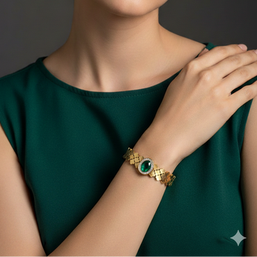 Woman wearing a gold bracelet with a green gemstone against a dark background