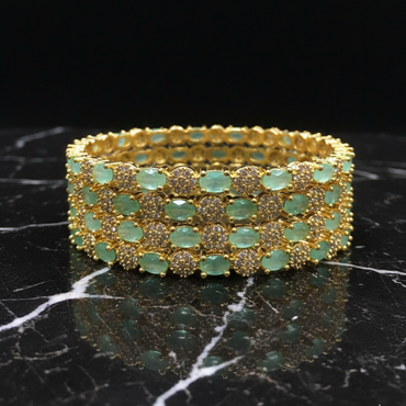 Gold bracelet with green gemstones on a black marble surface