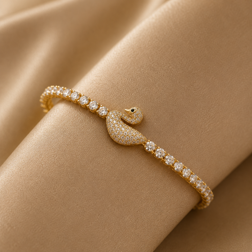 Gold-tone CZ pave swan tennis bracelet with fully micro-pave set swan centerpiece featuring black CZ eye and round CZ tennis chain displayed on champagne satin fabric