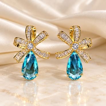 Gold-tone bow earrings with clear baguette-shaped accents, round sparkling centres and faceted blue teardrops