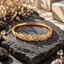 Gold-tone monogram-inspired bangle with sparkling clear crystals, floral motifs and polished gold finish