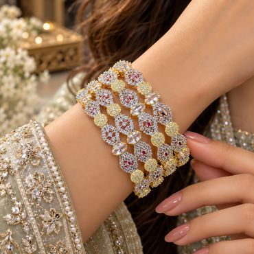 Model wearing four stacked gold-tone AD bangles with floral accent clusters, oval clear details and smaller round accent links.
