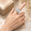Silver-tone CZ pave 5-petal flower cocktail statement ring with round and baguette cut white CZ petals and pave centre cluster on hand displayed on champagne satin with jewelry gift box and dried white flowers