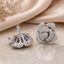 Silver-tone fully CZ pave rose flower stud earrings with 3D layered blooming petals and micro white cubic zirconia stones showing front and reverse hollow filigree view on champagne satin