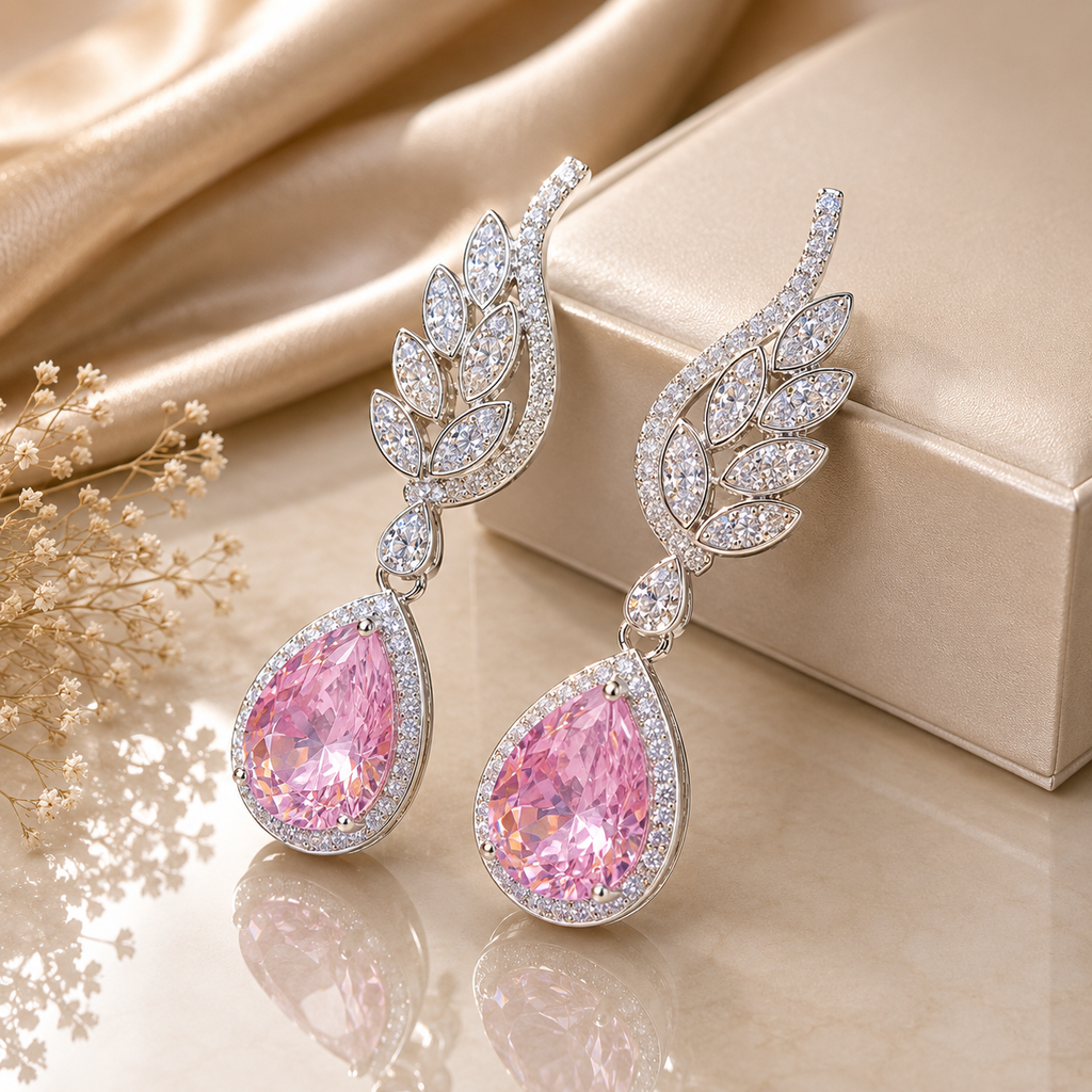 Silver-tone pink CZ teardrop and marquise leaf wing drop earrings featuring large pear-cut blush pink CZ center stone in round CZ halo frame with sweeping marquise and round CZ pave leaf wing top displayed on champagne satin with dried white flowers