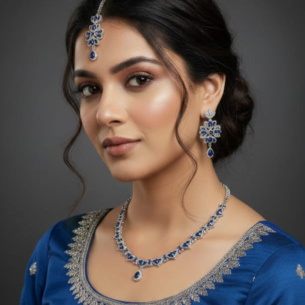 Woman wearing a blue traditional outfit with silver embroidery and jewelry against a dark background