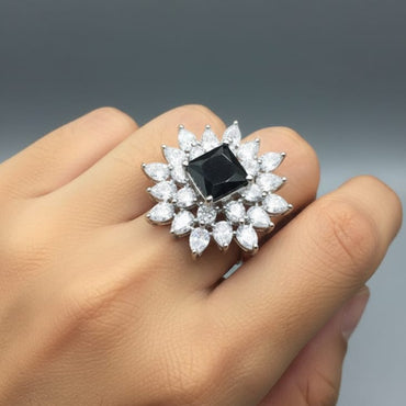 Ring with a central black gemstone and diamond-studded band on a hand against a gray background