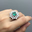 Ring with emerald and diamonds on a hand against a gray background