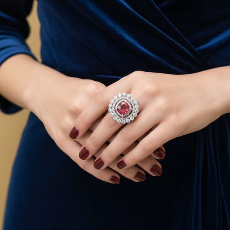 Person wearing a blue dress with a ring featuring a red gemstone, set against a blurred background.