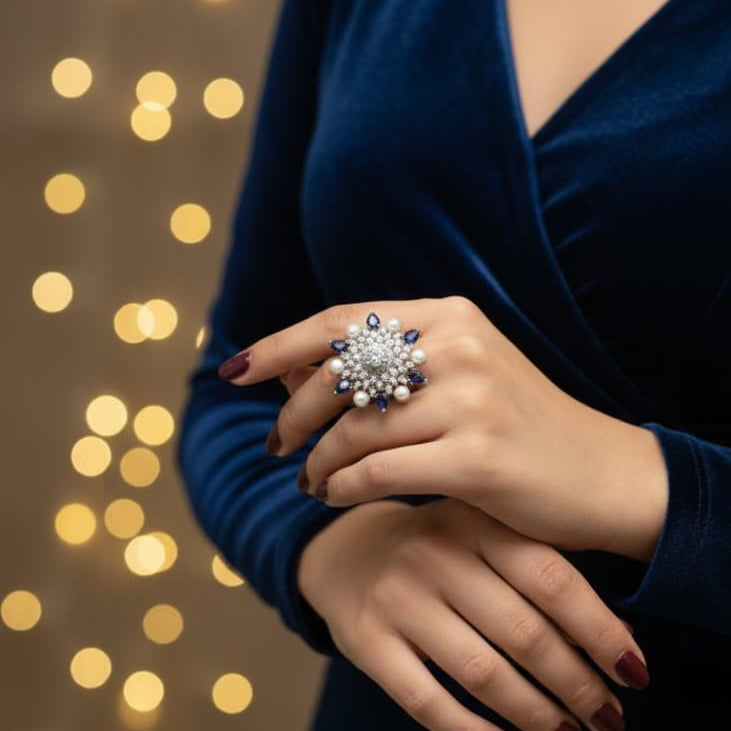 Person wearing a blue dress with a close-up of a hand holding a decorative ring against a blurred light background.