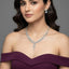 Woman wearing a purple off-shoulder dress with a diamond necklace and earrings on a gray background