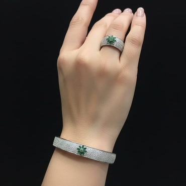Hand wearing a silver ring and bracelet with green gemstones on a black background