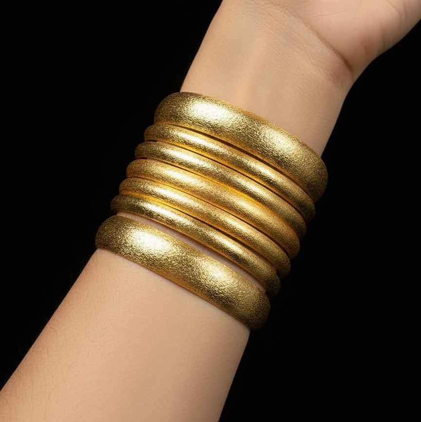 Gold bangles on a wrist against a black background