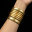 Gold bangles on a wrist against a black background
