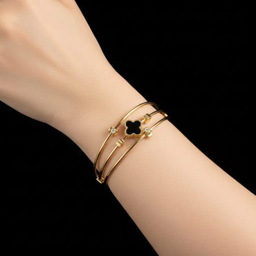 Gold bracelet with a clover design on a wrist against a black background