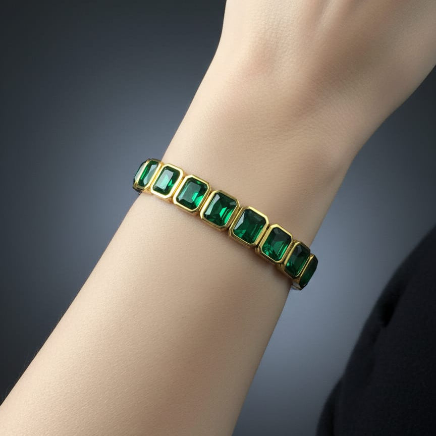 Gold bracelet with green gemstones on a wrist against a dark background