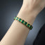 Gold bracelet with green gemstones on a wrist against a dark background