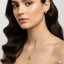 Woman wearing a gold heart-shaped necklace and earrings against a neutral background